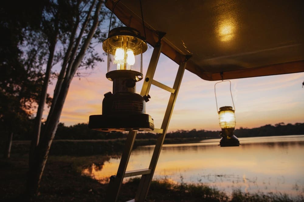 A lantern-lit camp shelter beside a lake at sunset