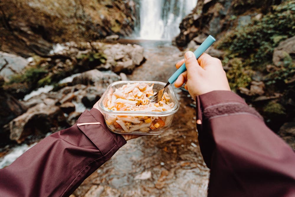 Illustrative stock photo: a pasta meal eaten outdoors beside a waterfall