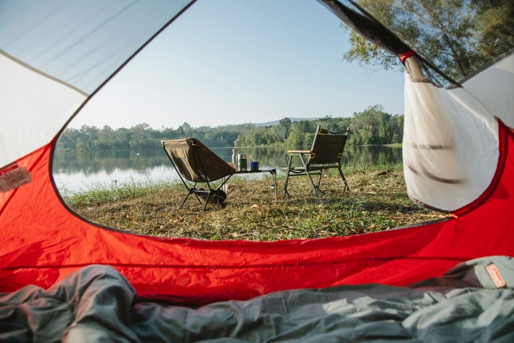 Illustrative stock photo: camp chairs beside a tent at a lakeside campsite