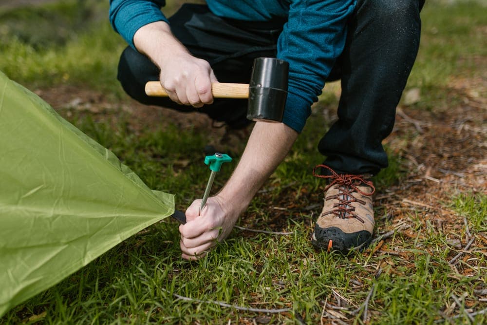 A hand hammering a tent stake into the ground