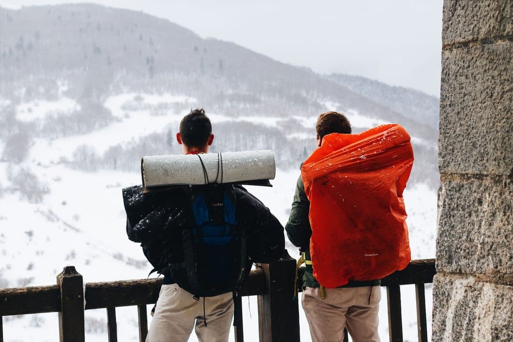Illustrative stock photo: two hikers with large backpacks looking at snowy mountains