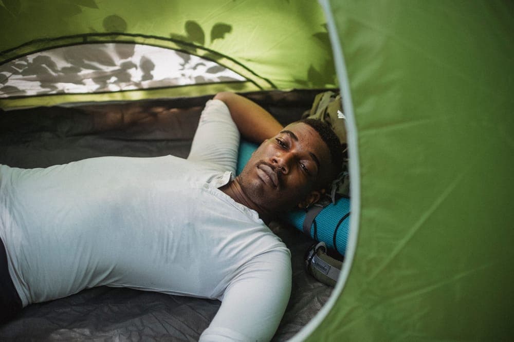 Illustrative stock photo: a hiker lying in a tent with a hand behind his head