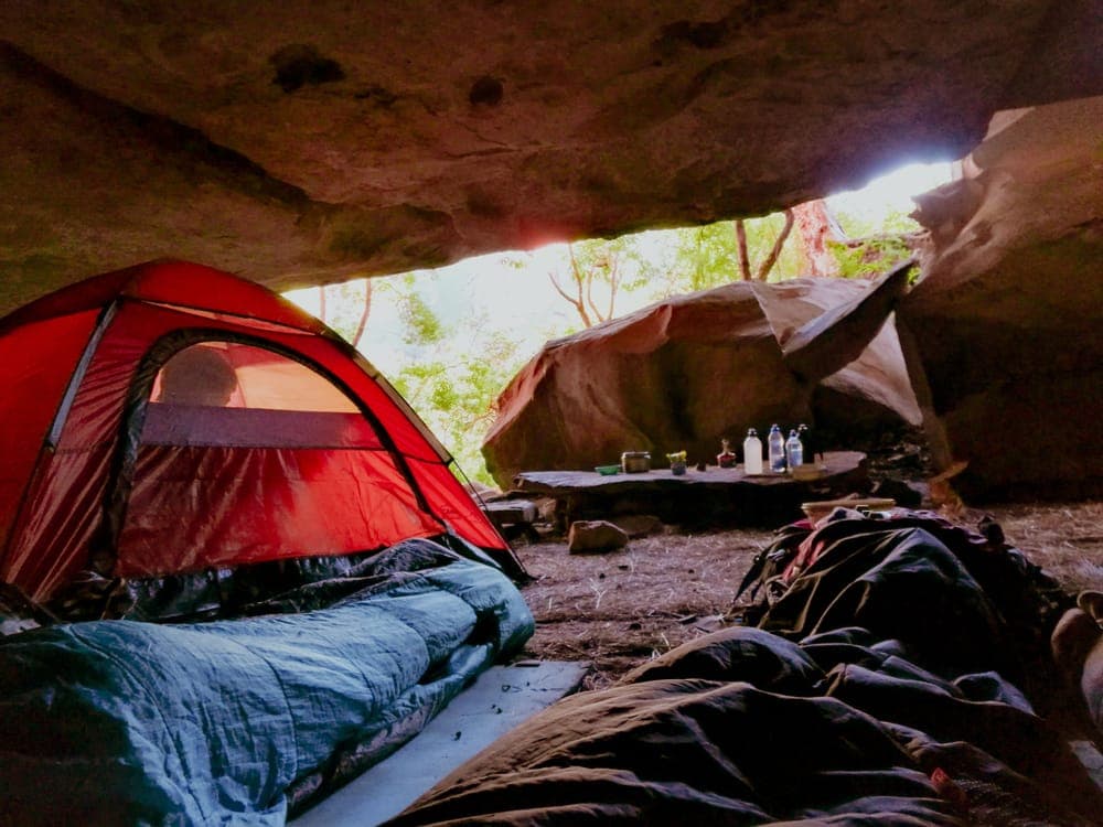 Illustrative stock photo: a red tent pitched in a rocky, sheltered campsite
