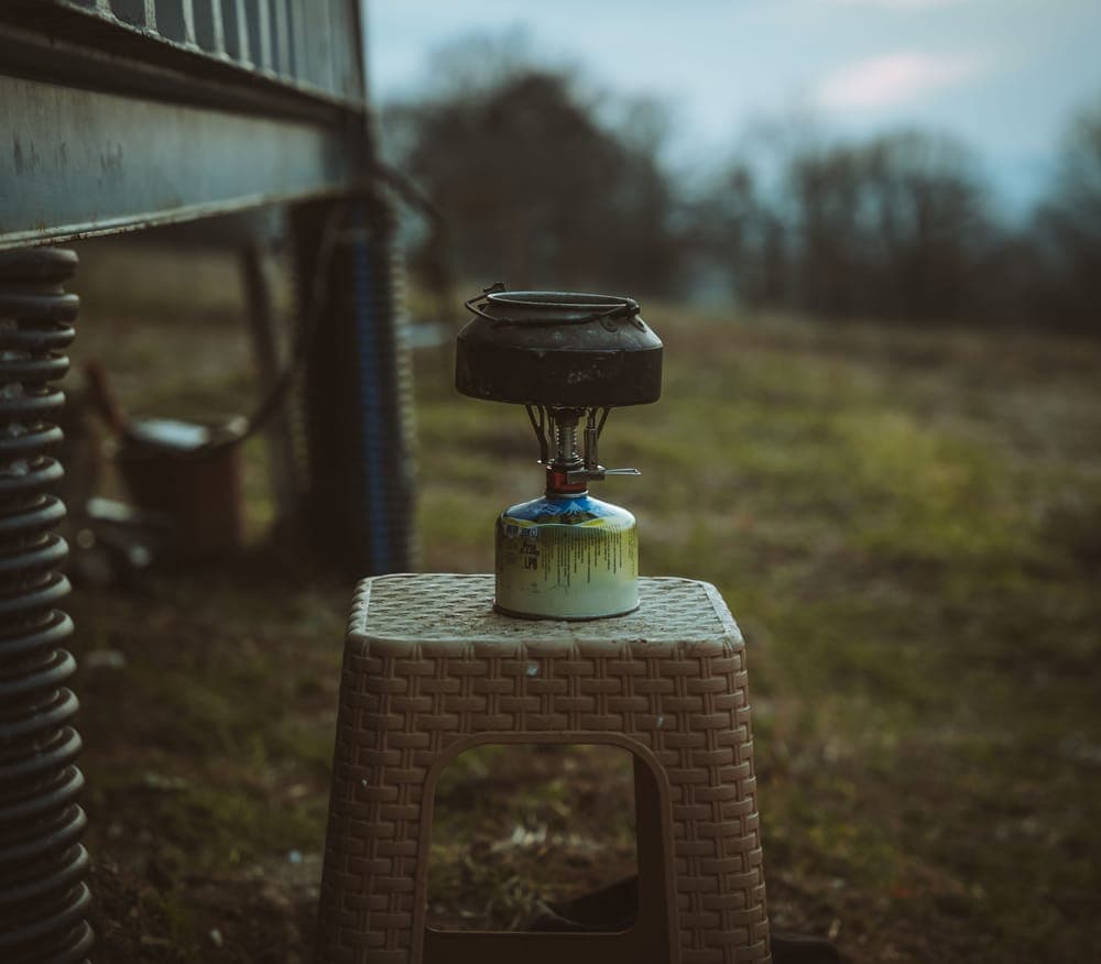 Illustrative stock photo: a small camping stove set on a stool in an open field