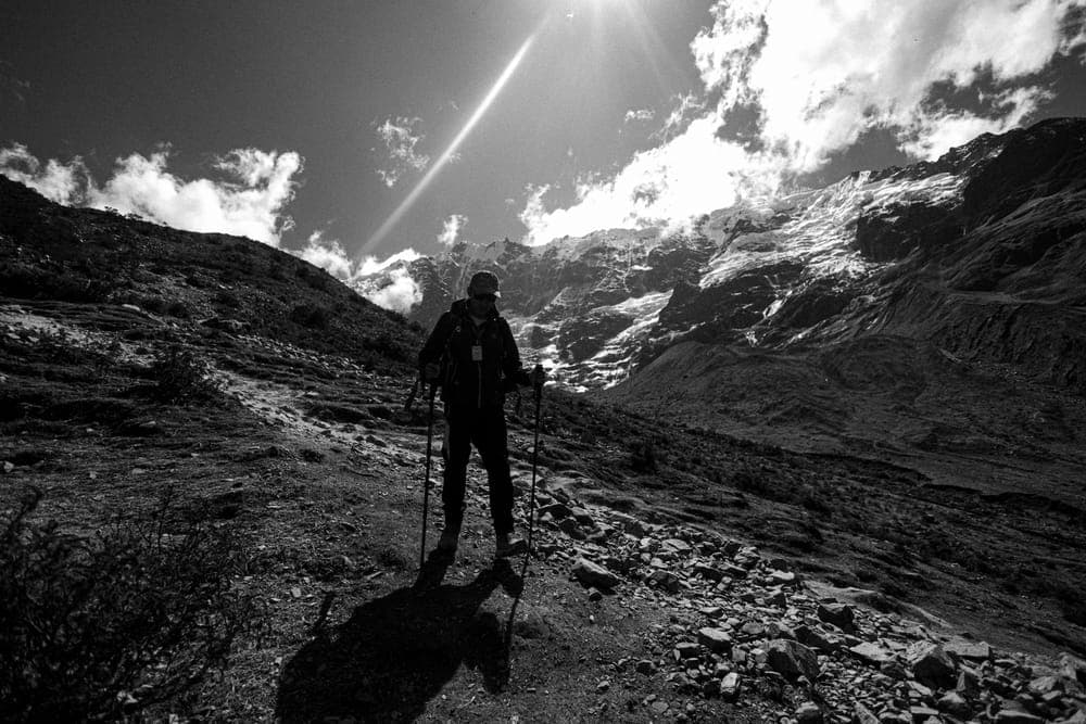 Illustrative stock photo: a hiker with trekking poles silhouetted on a rocky mountain path